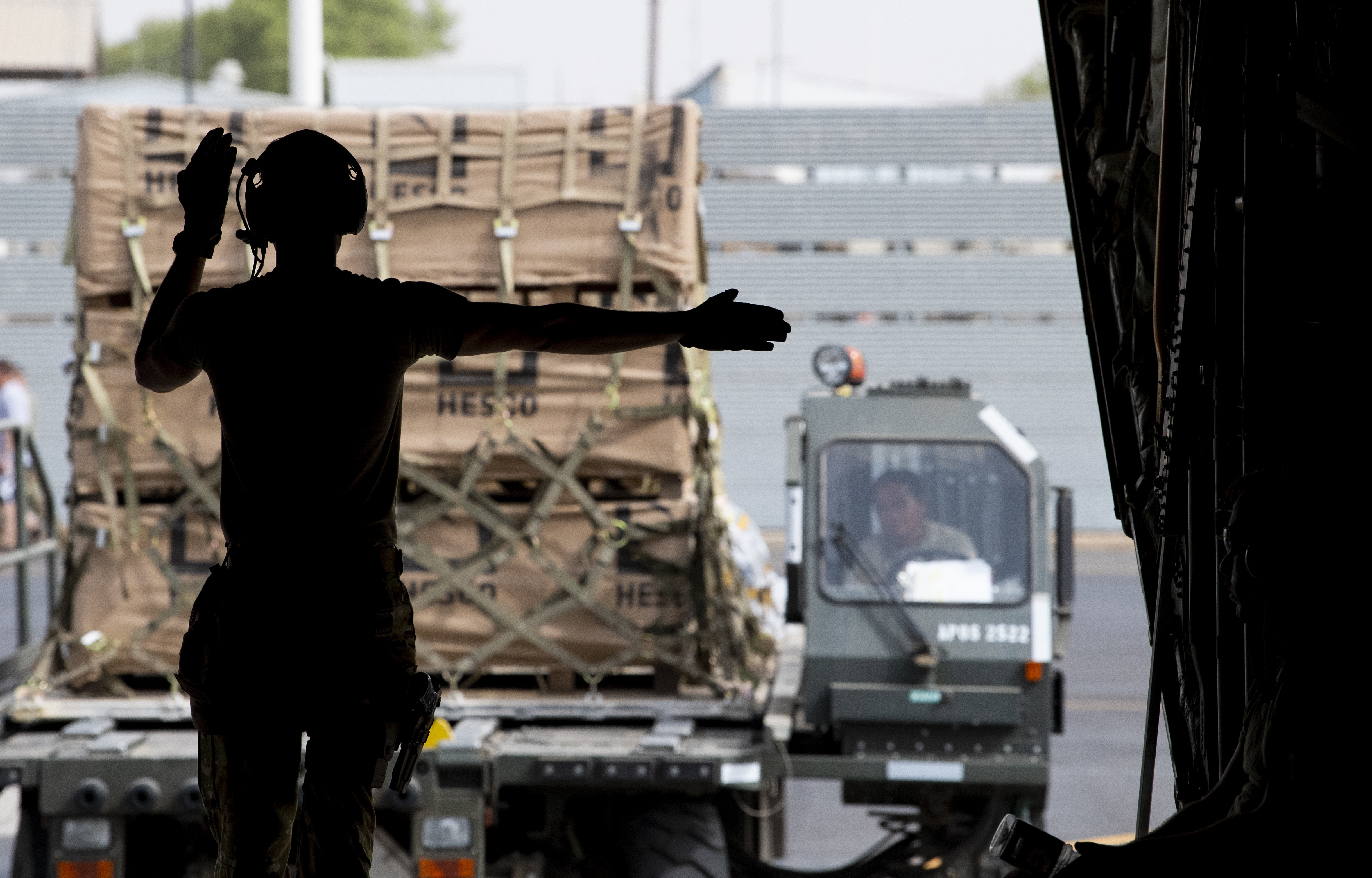 A service member directs material handling equipment loaded with cargo onto the ramp of an aircraft. 